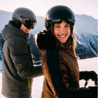 2 people on top of a ski slope. A women is smiling at the camera